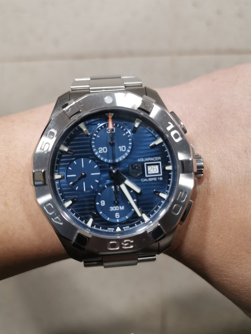 A close-up of a TAG Heuer Aquaracer watch with a blue dial and steel bracelet on a person's wrist.