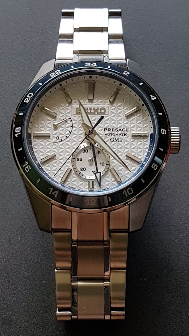 A close-up shot of a silver Seiko Presage Automatic GMT watch with a textured white dial.