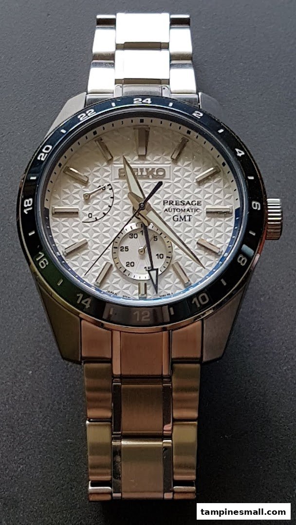A close-up shot of a silver Seiko Presage Automatic GMT watch with a textured white dial.