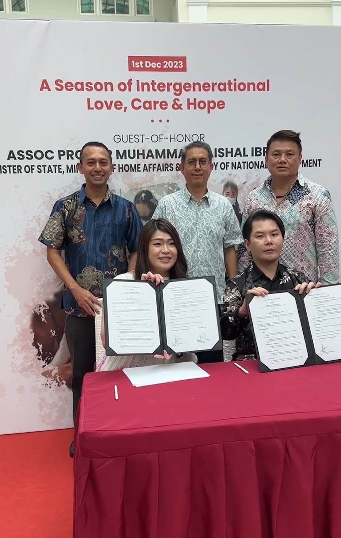 Individuals, including a guest of honor, sign documents at an event themed 'A Season of Intergenerational Love, Care & Hope'.