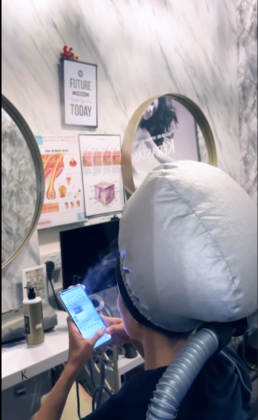 A customer relaxing during a hair treatment with a steamer at Vintage Studio VS Salon.