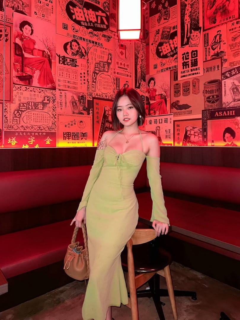 A person in a light green dress poses inside a salon with vintage Chinese-themed decor and red lighting.