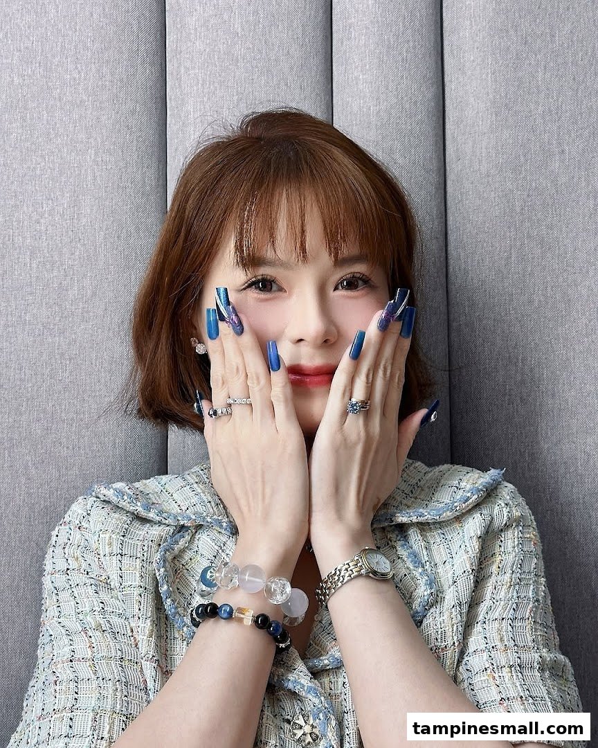 A woman showcasing long, blue manicured nails with intricate designs, wearing rings and bracelets.