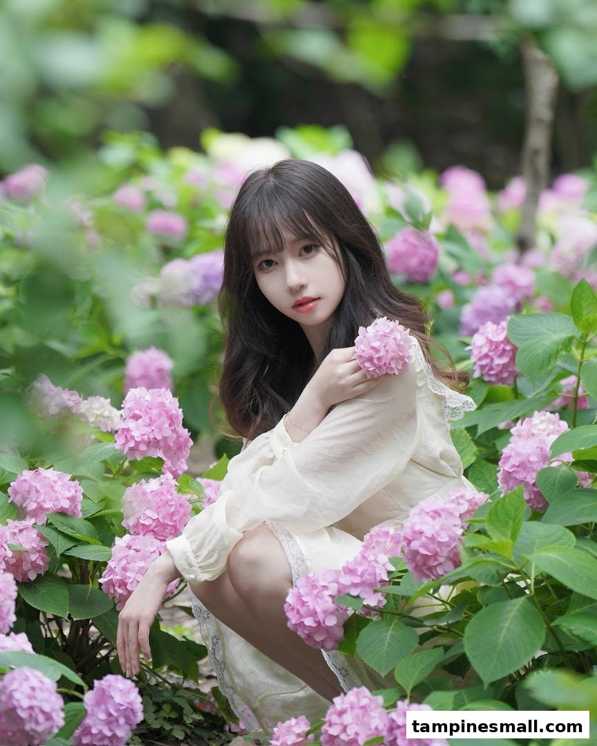 A young woman in a field of pink hydrangeas, embodying natural beauty and freshness.