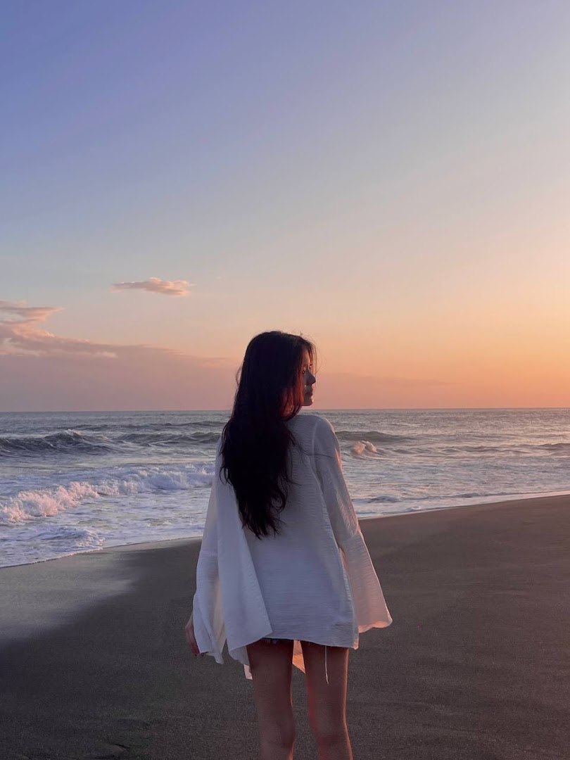 A person stands on a beach at sunset, looking out at the ocean waves.