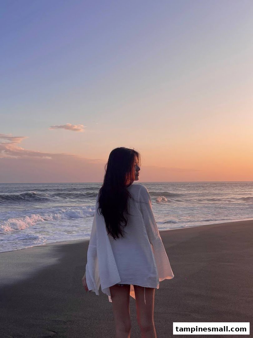A person stands on a beach at sunset, looking out at the ocean waves.