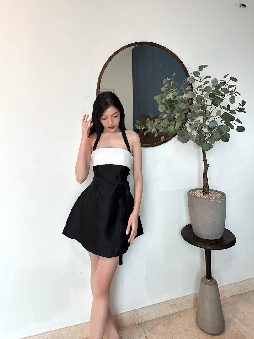A woman in a stylish black and white dress poses in a modern interior with a mirror and plant.