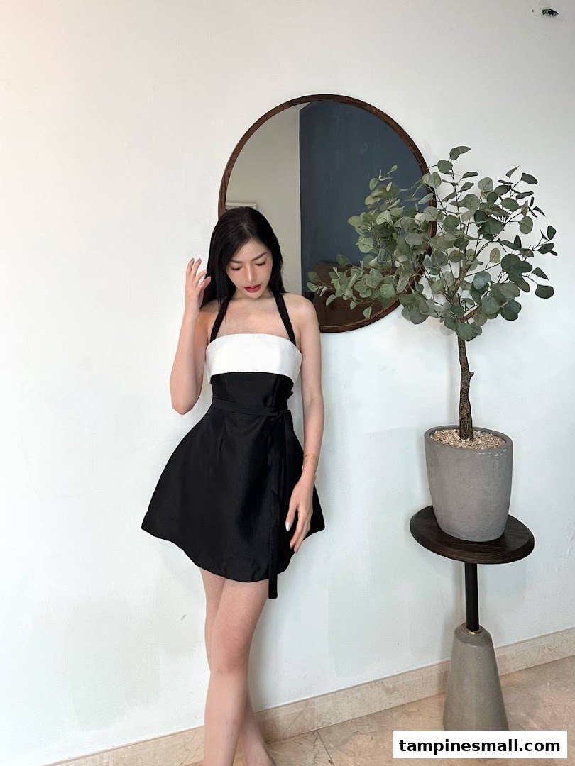 A woman in a stylish black and white dress poses in a modern interior with a mirror and plant.