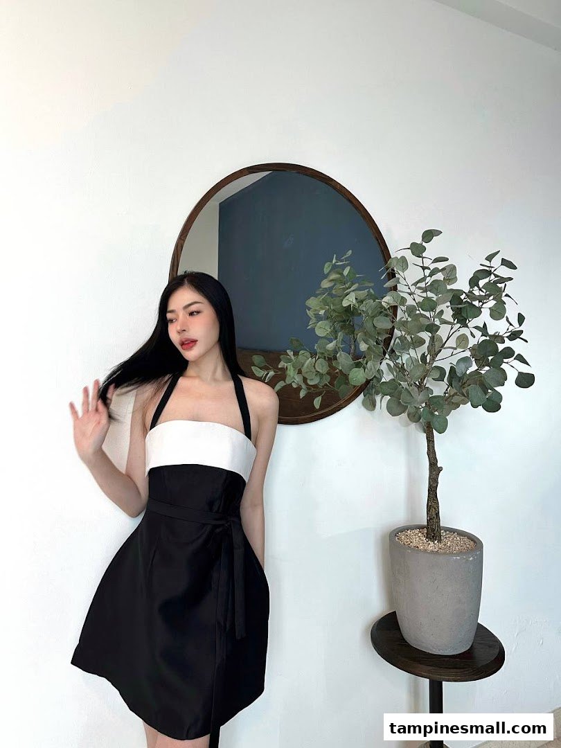 A woman in a black and white dress posing in a stylish interior with a mirror and plant.