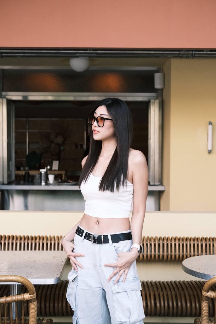 A stylish woman stands outside a modern salon or studio, featuring outdoor seating.