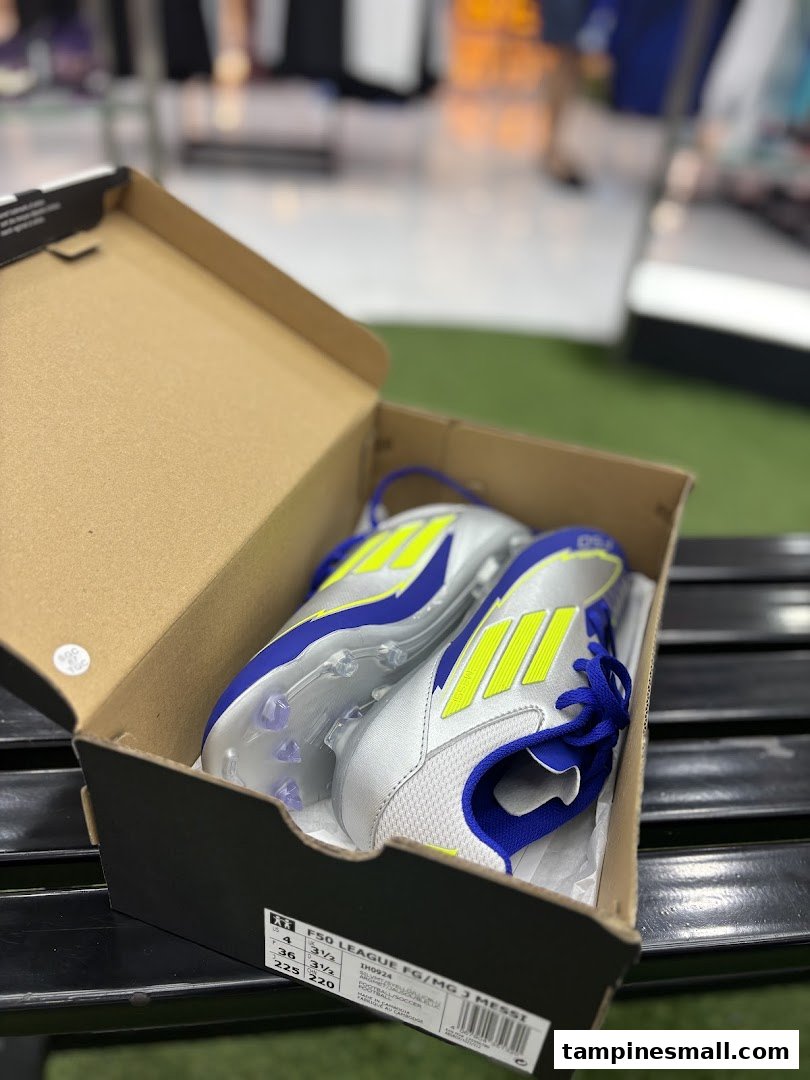 A pair of new silver, blue, and neon yellow soccer cleats in an open box.