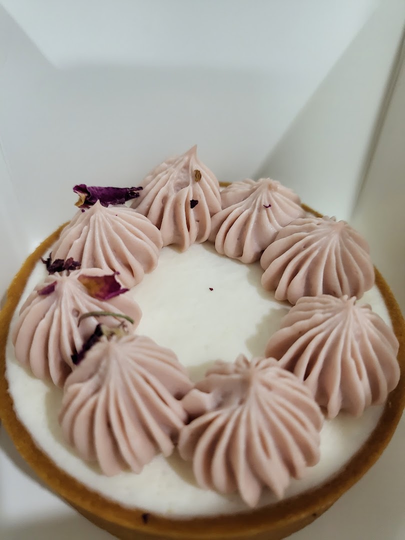 A close-up of a delicate tart with light purple cream swirls and dried rose petals.