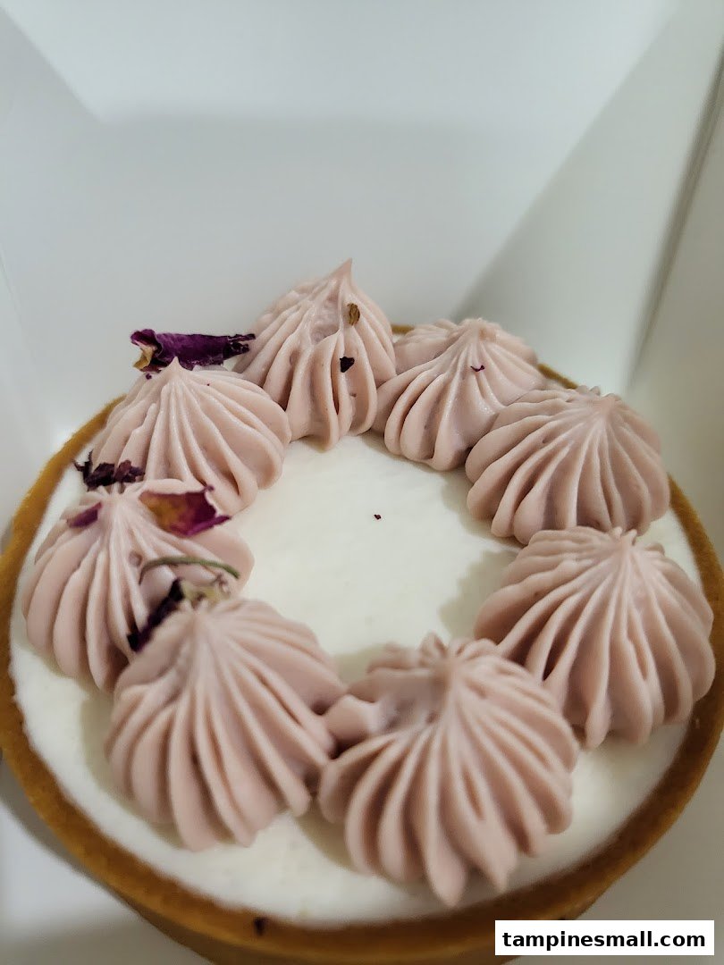 A close-up of a delicate tart with light purple cream swirls and dried rose petals.