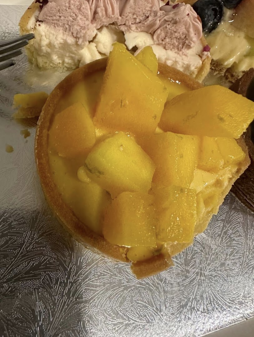 A close-up of a vibrant mango tart with fresh mango chunks, alongside another delicate pastry.