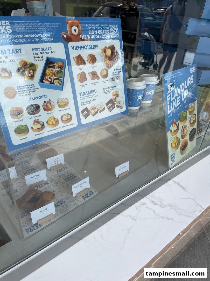 A display of pastries, tarts, and viennoiseries with menu boards visible through the shop window at Wunderfolks.
