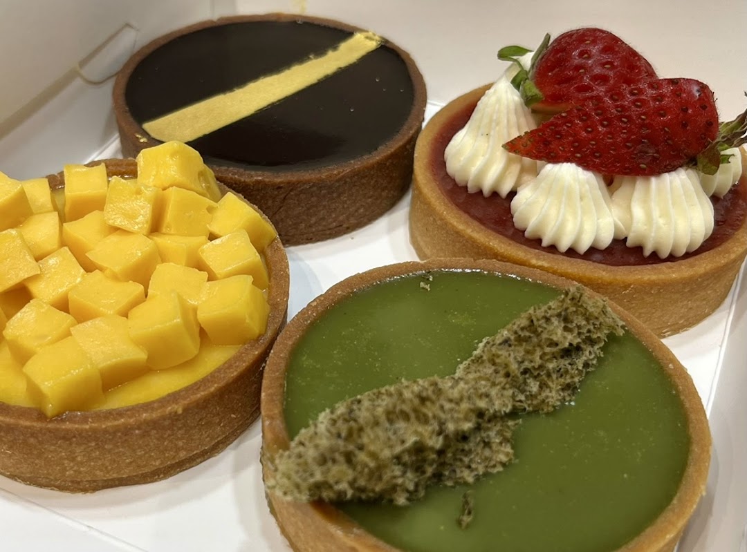 A close-up of four colorful tarts, including mango, chocolate, strawberry, and matcha flavors.