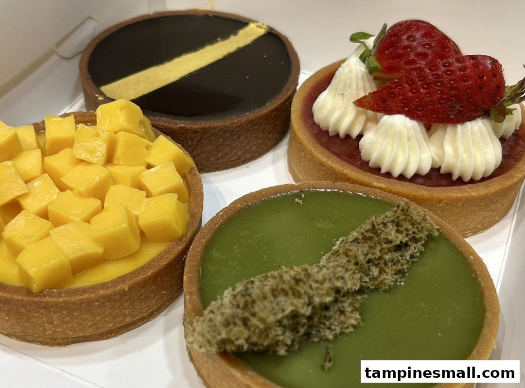 A close-up of four colorful tarts, including mango, chocolate, strawberry, and matcha flavors.