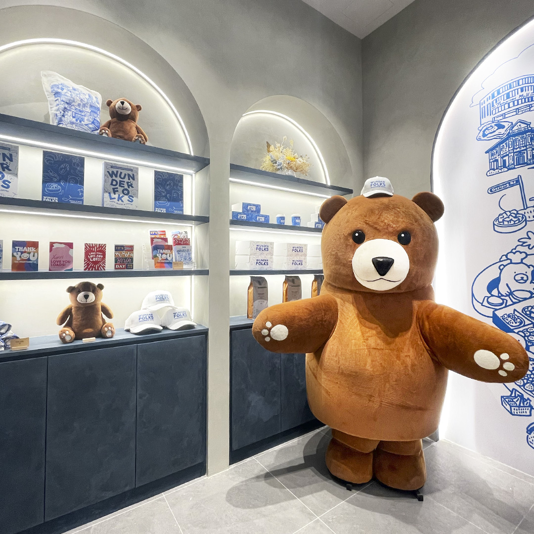 A large bear mascot stands inside Wunderfolks Pastry and Coffee, surrounded by branded merchandise.