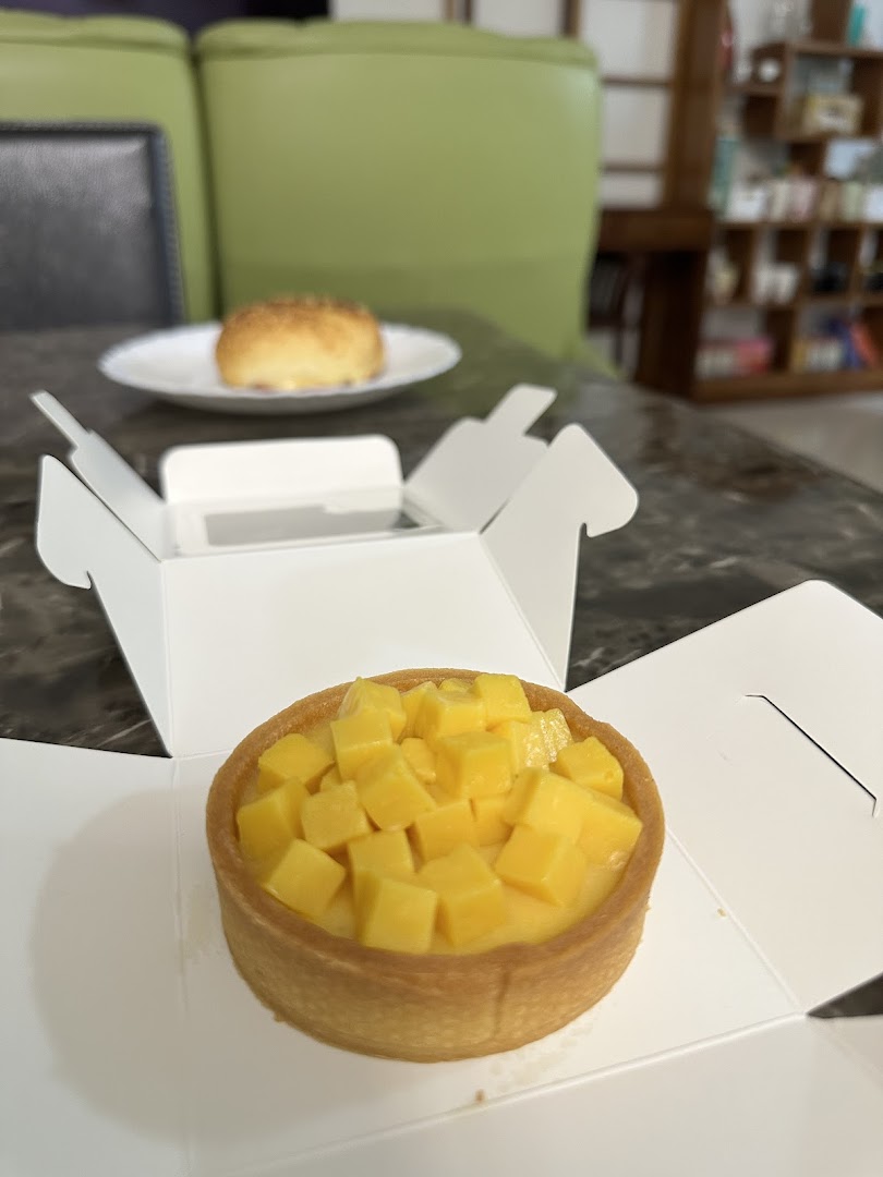 A vibrant mango tart in an open box, with another pastry on a plate in the background.