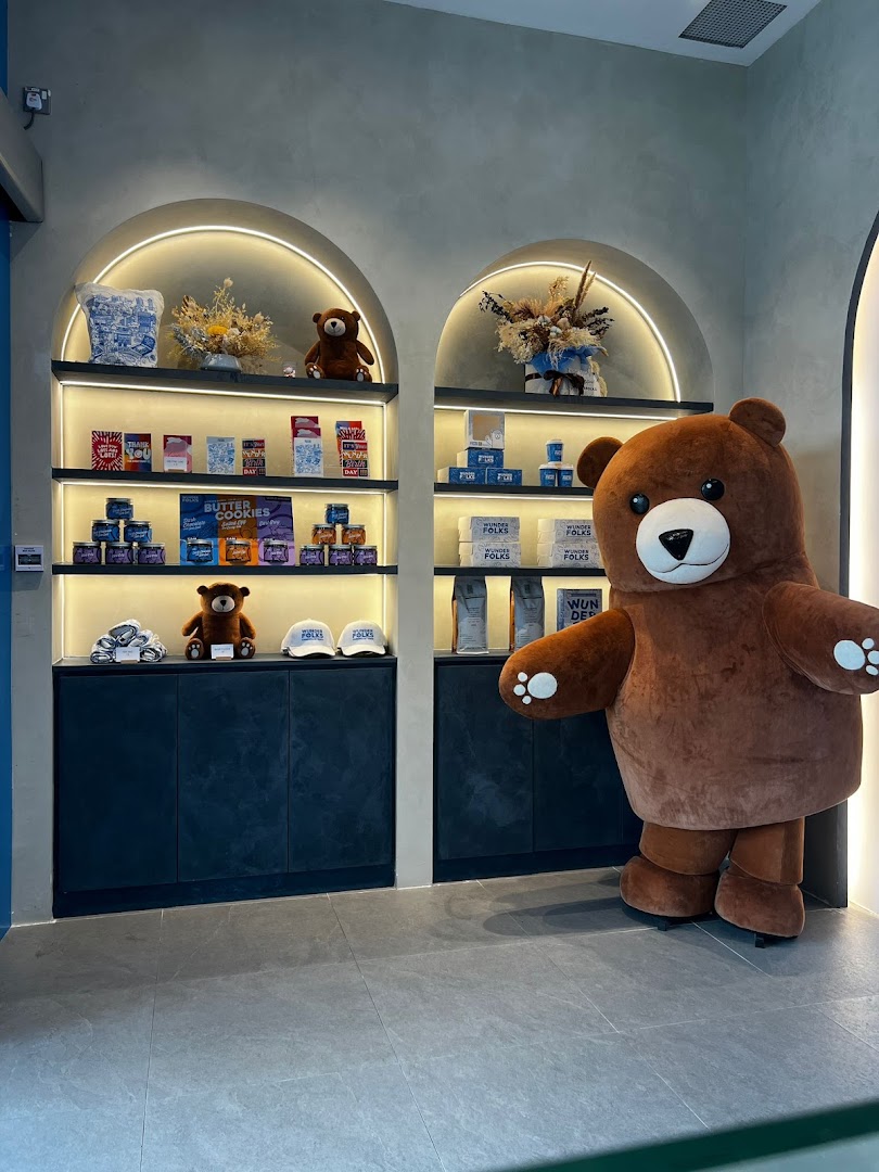 A large bear mascot stands beside shelves displaying merchandise and gifts inside Wunderfolks Pastry and Coffee.
