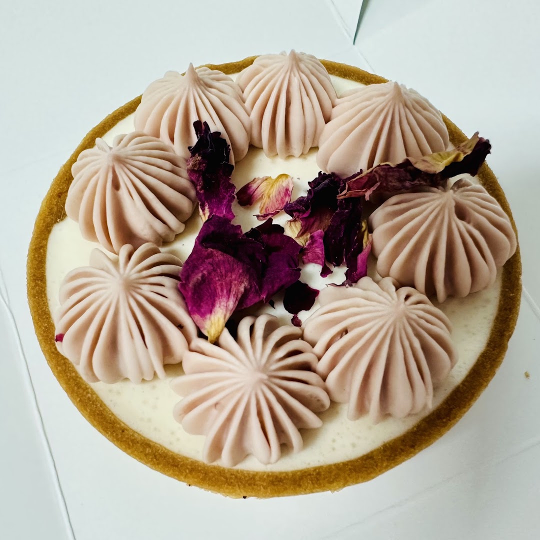 A beautifully decorated round tart or cake featuring cream swirls and dried rose petals.