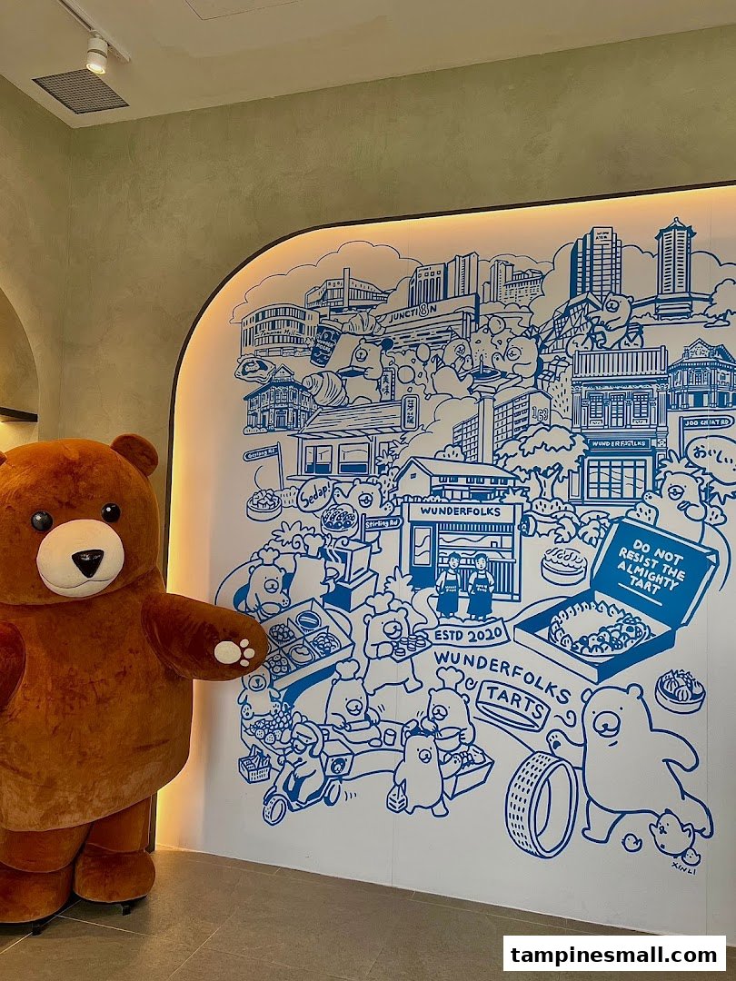 A large bear mascot stands beside a whimsical blue and white mural depicting cityscapes and bear characters.