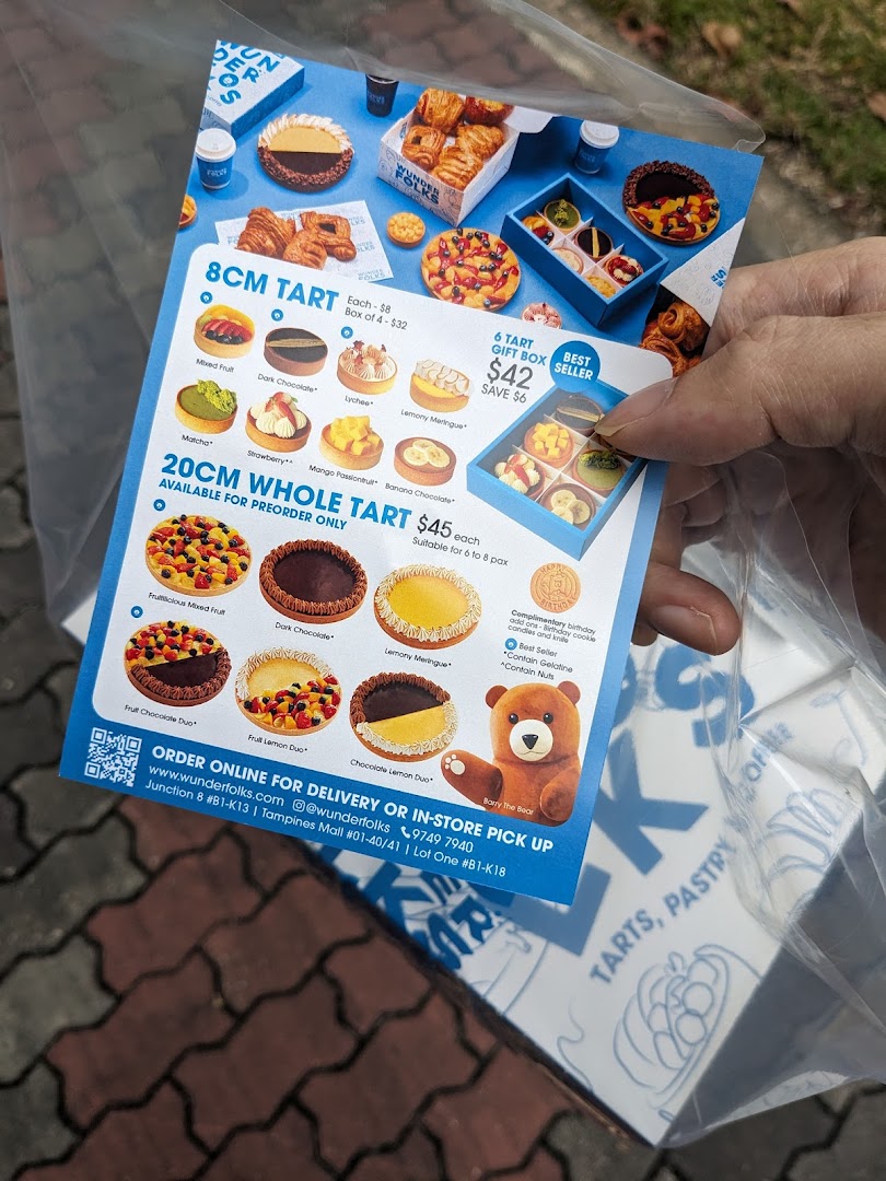 A hand holds a flyer showcasing various tarts and pastries from Wunderfolks, including pricing and ordering information.