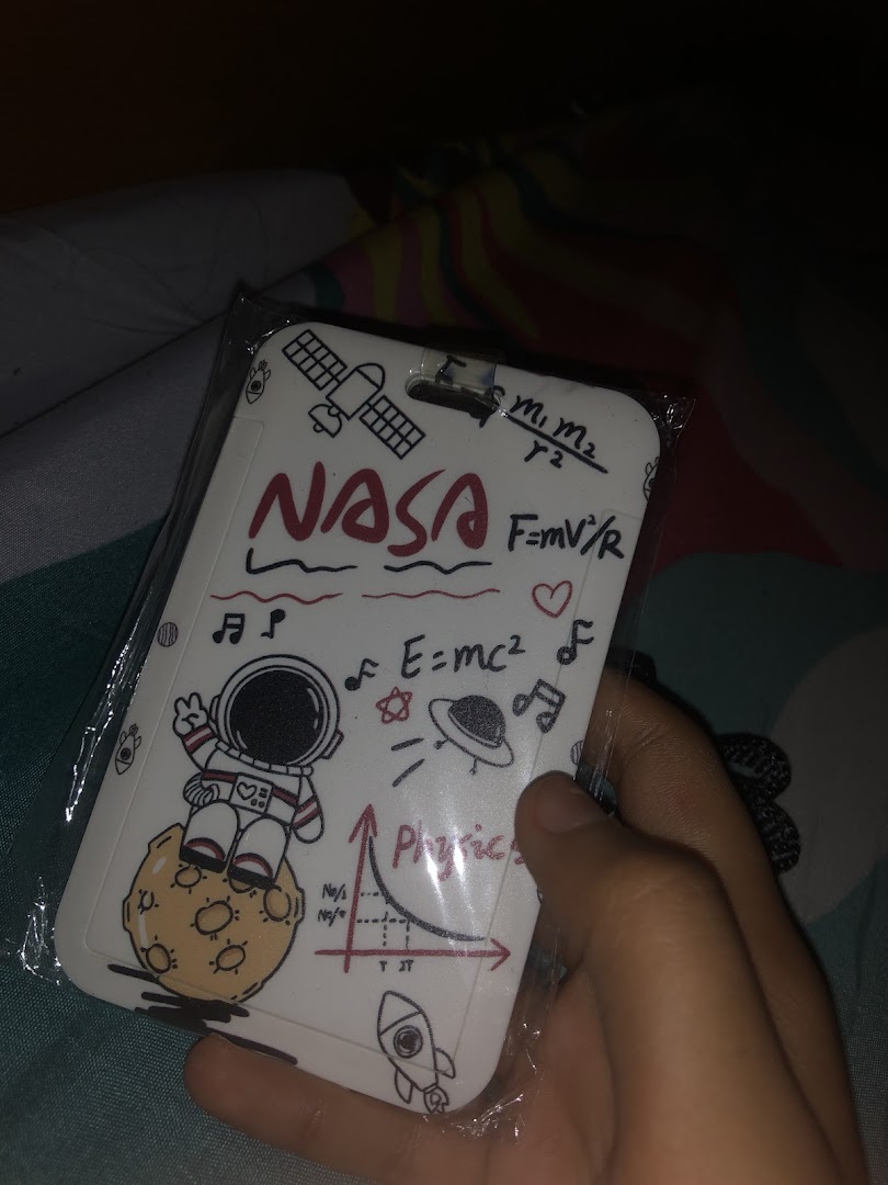 A hand holds a white card holder featuring NASA, astronaut, and physics-themed doodles.