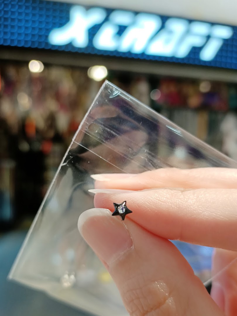 A hand holds a star-shaped piercing in a plastic bag, with the X-Craft shop logo in the background.