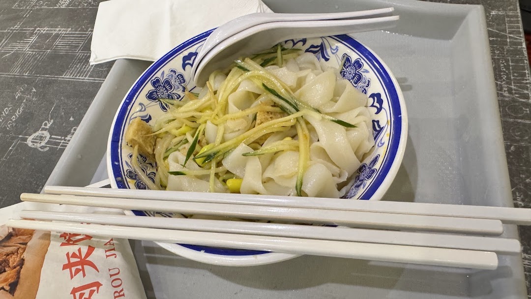 A delicious bowl of wide noodles with cucumber and tofu, served with chopsticks and spoon.