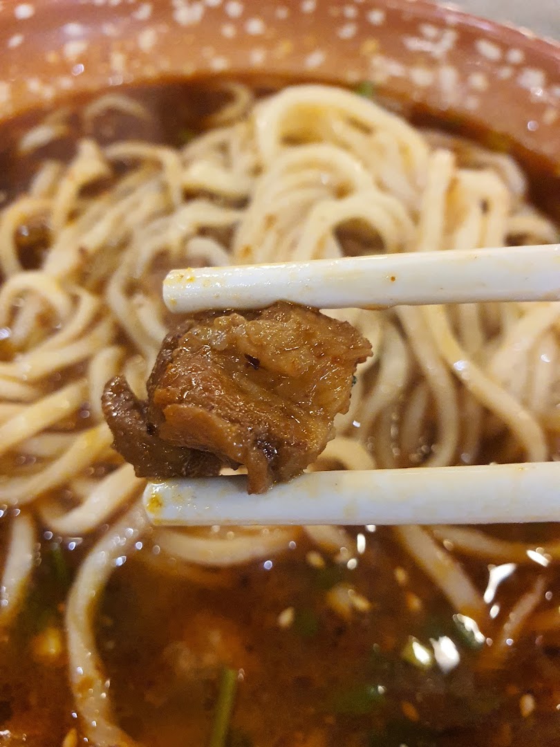 Close-up of a tender meat piece held by chopsticks over a bowl of savory noodles.