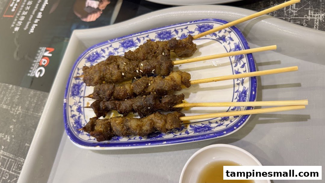 A plate of five grilled meat skewers with sesame seeds, served with a dipping sauce.