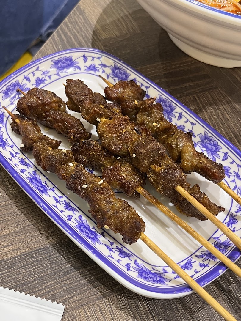 Close-up of several grilled meat skewers on a decorative white and blue plate.