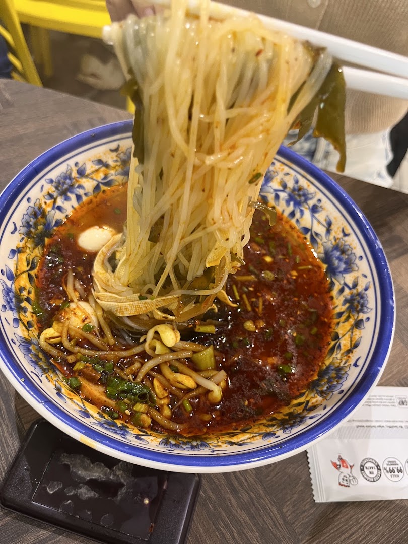 Chopsticks lifting spicy noodles from a decorative bowl at XiAn Impression.
