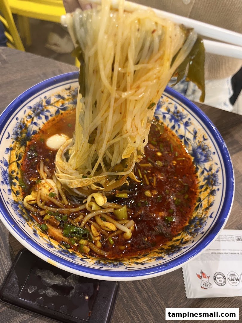Chopsticks lifting spicy noodles from a decorative bowl at XiAn Impression.