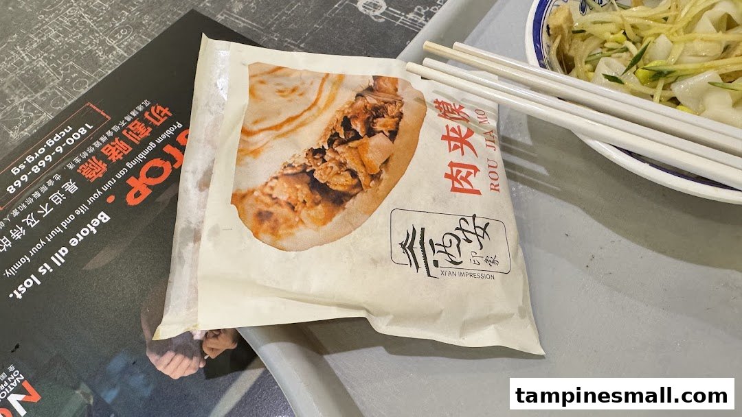 A Rou Jia Mo in a branded wrapper and a bowl of noodles on a tray, showcasing Xi'an Impression's cuisine.