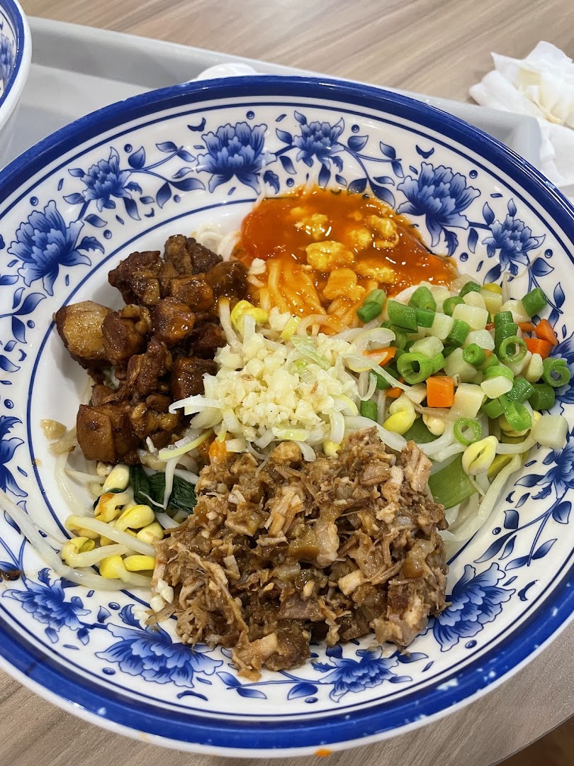 A vibrant bowl of Xian noodles with braised pork, minced meat, fresh vegetables, and spicy sauce.