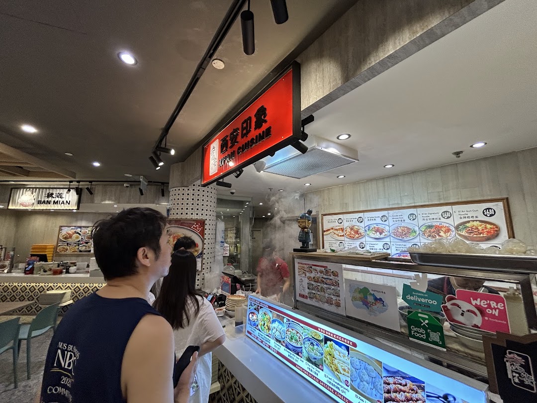 Customers queueing at the counter of Xian Cuisine, a food stall with menu displays.