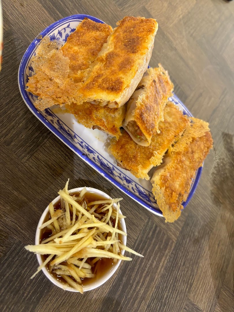 Crispy pan-fried dumplings served with a ginger and vinegar dipping sauce on a decorative plate.