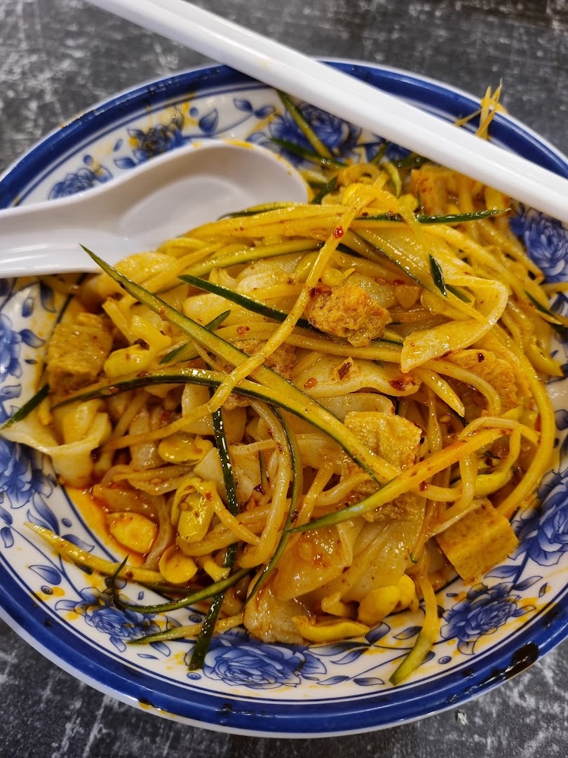 A vibrant bowl of spicy Xian-style noodles with cucumber and other ingredients in a decorative bowl.