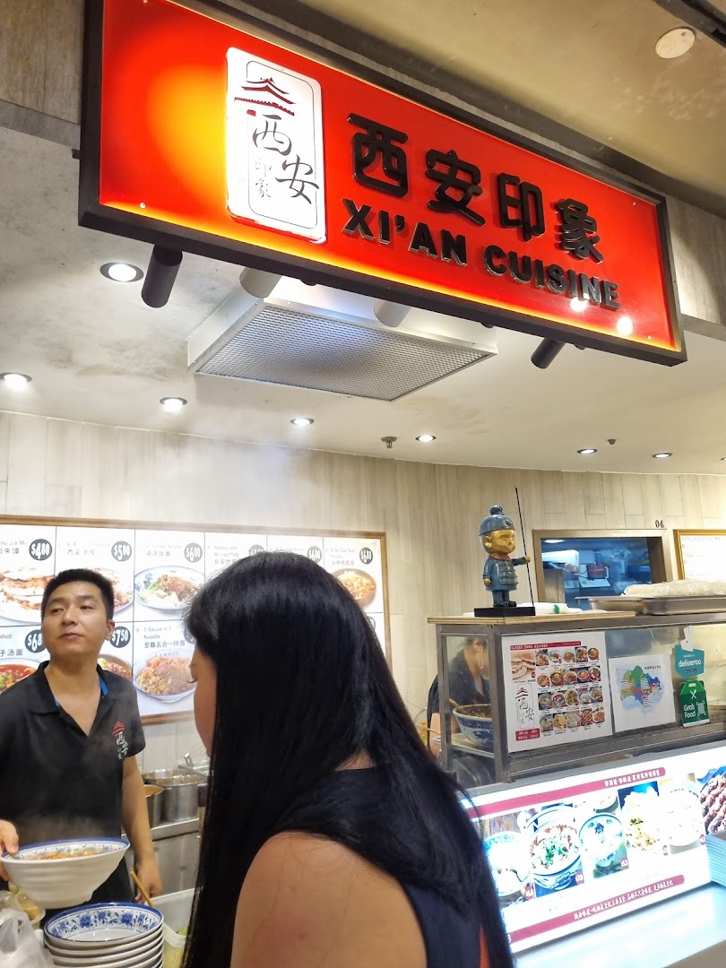 A staff member serves a customer at the counter of Xi'an Cuisine, showcasing the shop's vibrant atmosphere.