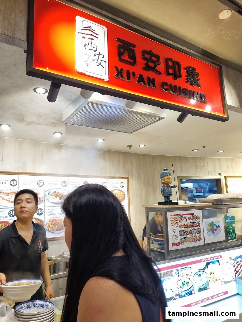 A staff member serves a customer at the counter of Xi'an Cuisine, showcasing the shop's vibrant atmosphere.