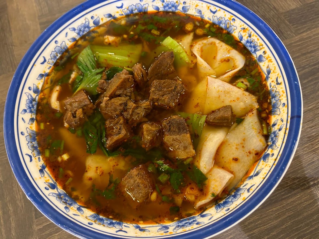 A vibrant bowl of Xian-style beef noodle soup with wide noodles and green vegetables.