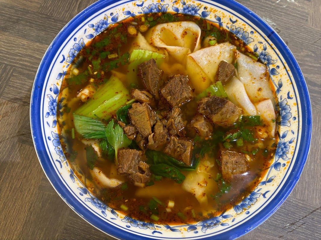 A vibrant bowl of spicy beef noodles with wide flat noodles and bok choy.