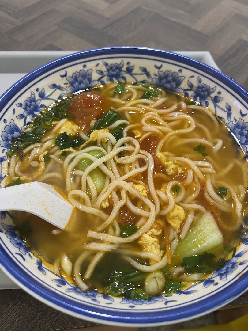 A close-up of a colorful bowl of Xian-style noodles with tomatoes, egg, and greens.