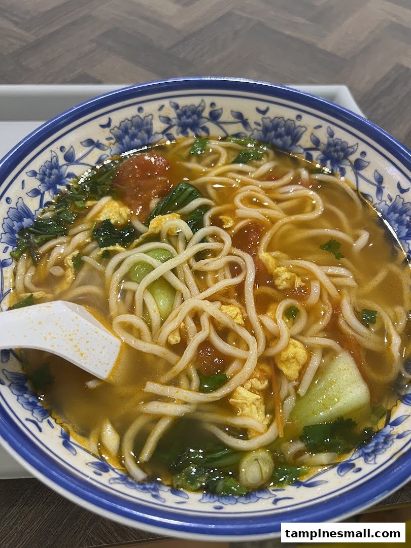 A close-up of a colorful bowl of Xian-style noodles with tomatoes, egg, and greens.