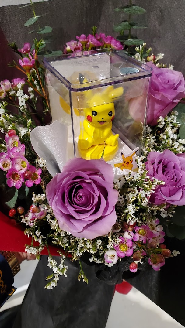 A vibrant floral bouquet featuring purple roses and a Pikachu figurine in a clear box.