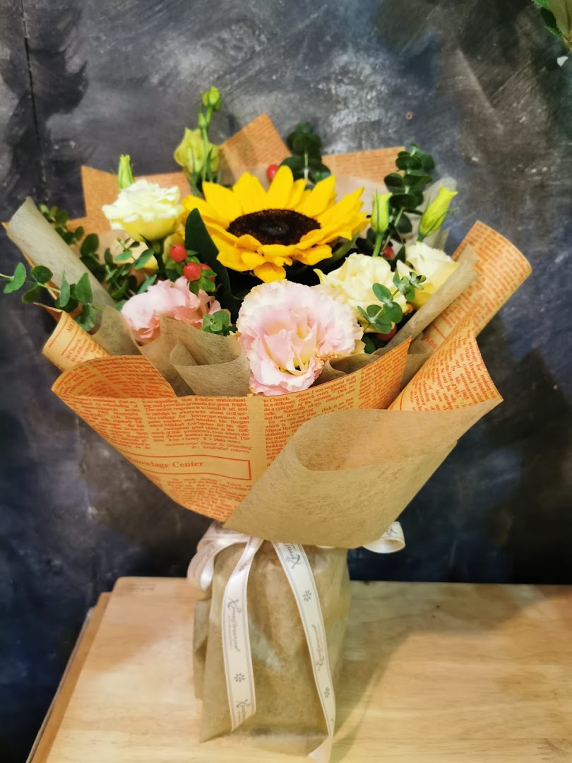 A vibrant bouquet featuring a sunflower, pink, and white flowers, beautifully wrapped in paper.