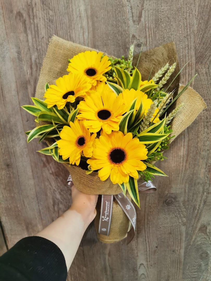 A hand holds a vibrant bouquet of yellow gerbera daisies wrapped in burlap.
