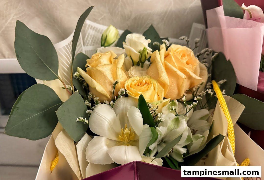 A vibrant bouquet featuring yellow roses, white tulips, and green foliage, presented in a gift bag.
